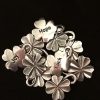 A cluster of silver four leaf clover charms with the words "Hope," "Luck," and "Joy" engraved on three of them, displayed against a black background.