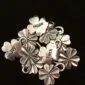 A cluster of silver four leaf clover charms with the words "Hope," "Luck," and "Joy" engraved on three of them, displayed against a black background.