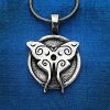 The Luna Moth Pendant, featuring swirling designs, hangs from a chain against a blue fabric background.