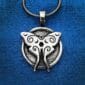 The Luna Moth Pendant, featuring swirling designs, hangs from a chain against a blue fabric background.
