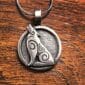 The Howling Wolf Pendant is a round silver piece featuring a stylized howling wolf and Celtic inspired spiral patterns, displayed on a wooden surface.