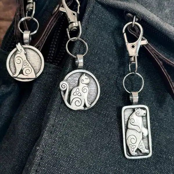 Howling Wolf Bag Charm – Celtic Spirals Collection The Howling Wolf Bag Charm from the Celtic Spirals Collection features intricate swirling patterns, adding a unique touch to any dark fabric bag.