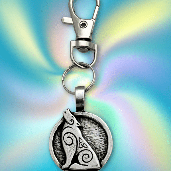 The Howling Wolf Bag Charm from the Celtic Spirals Collection features a silver keychain with a circular pendant of an engraved wolf howling on a vibrant blue and yellow background—ideal as a unique charm for bags or backpacks.