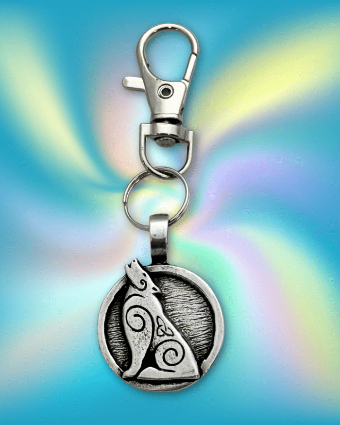 The Howling Wolf Bag Charm from the Celtic Spirals Collection features a silver keychain with a circular pendant of an engraved wolf howling on a vibrant blue and yellow background—ideal as a unique charm for bags or backpacks.