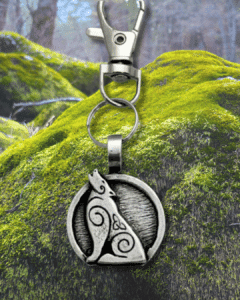The Howling Wolf Bag Charm from the Celtic Spirals Collection features a silver keychain with a circular pendant of a howling wolf and Celtic swirls, perfect for accessorizing bags or keys against any forest-inspired backdrop.