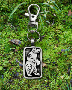 The Standing Bear Bag Charm from the Celtic Spirals Collection features an engraved bear with spiral designs, resting on green moss and leaves—perfect as a unique bag bauble.