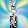 The Standing Bear Bag Charm from the Celtic Spirals Collection features a silver rectangular pendant with an engraved bear, swirling and Celtic knot designs, and a vibrant multicolored background—a unique adornment for bags or keys.