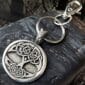 A Celtic Tree of Life Bag Charm with a circular pendant and silver keyring rests on a textured dark rock surface. The lobster clasp is attached to the pendant’s loop.